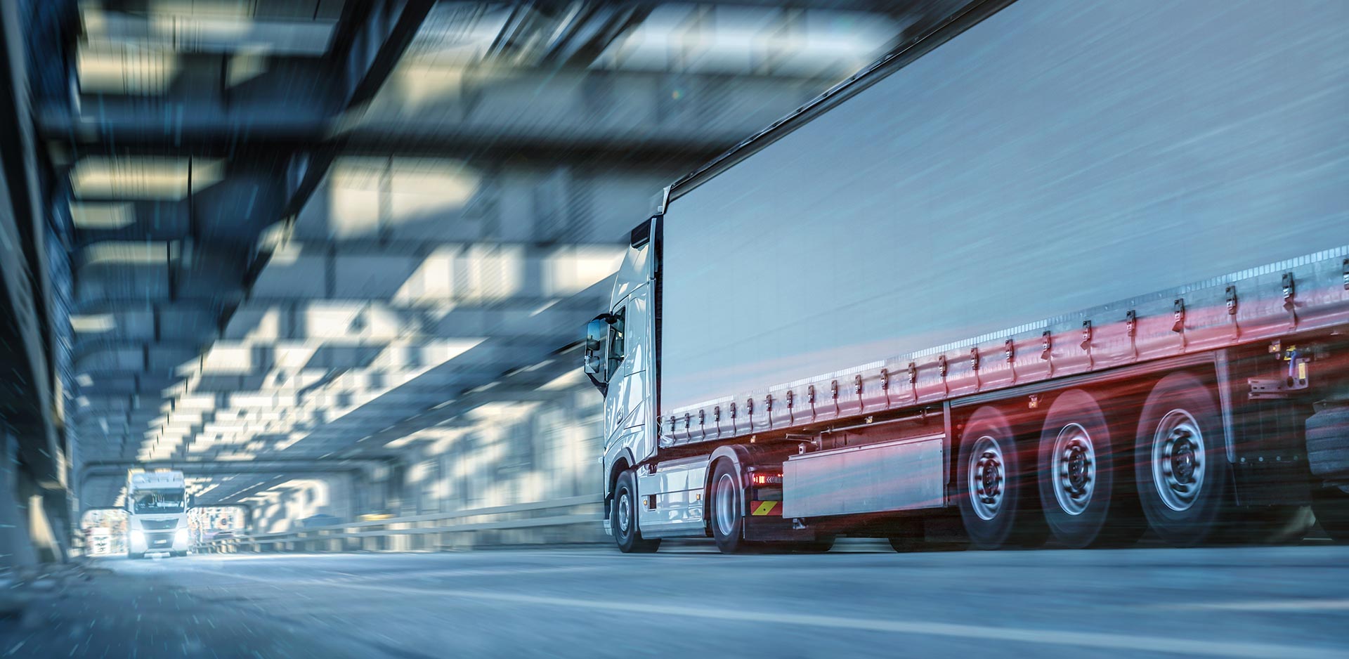 Ein LKW fährt schnell durch einen Tunnel, links im Bild ist ein weiterer LKW im Hintergrund.